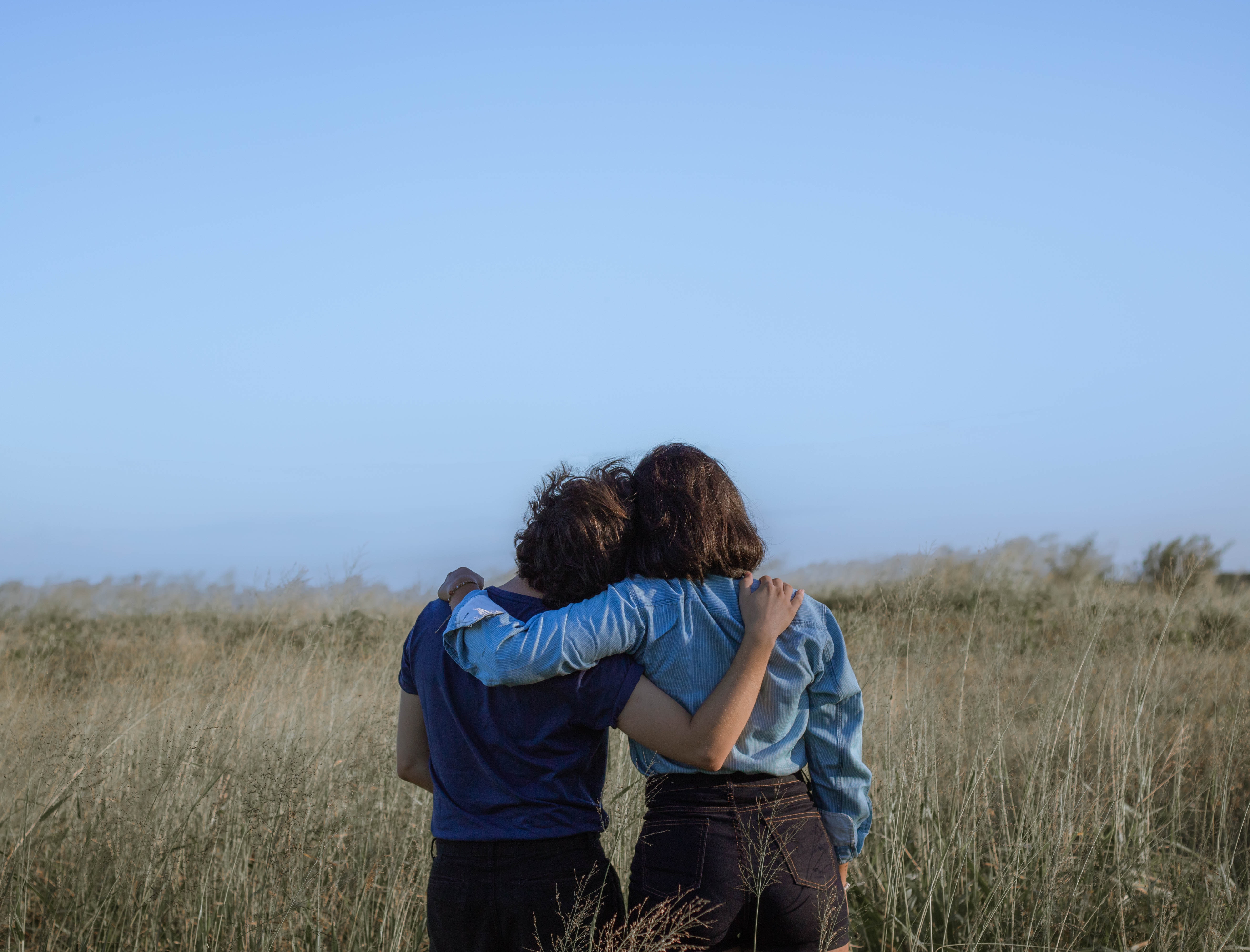 Two friends with arms around each other looking over a field of grass